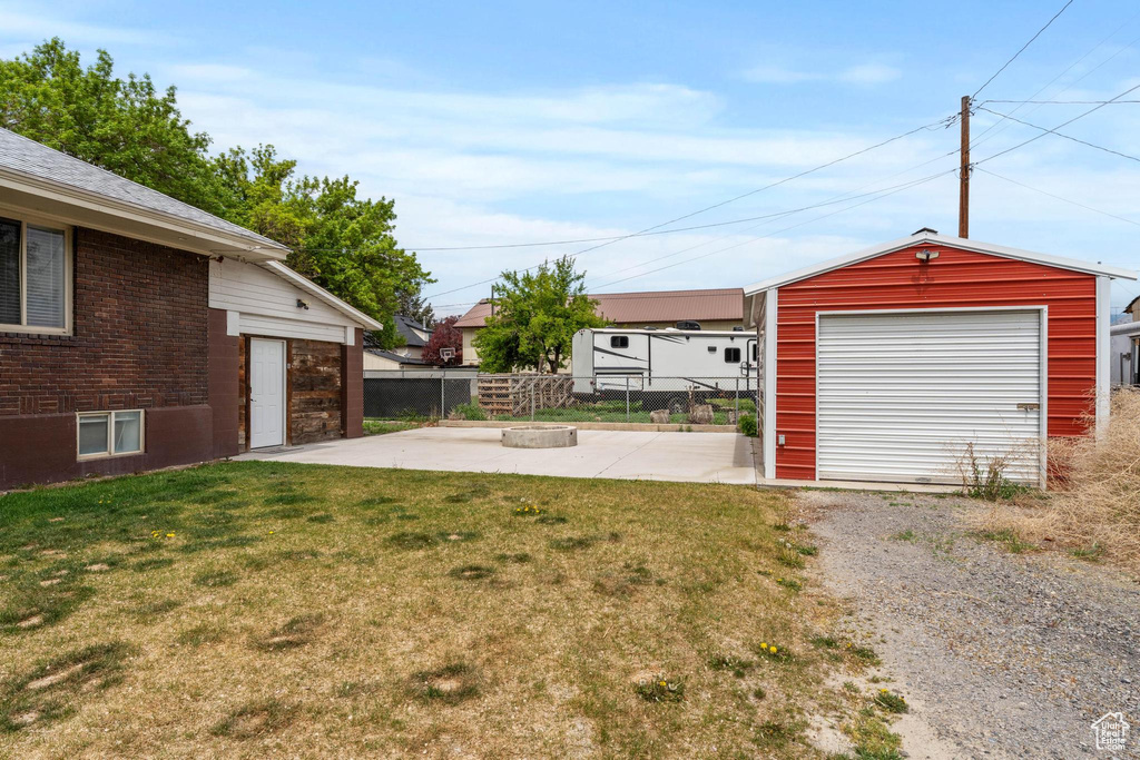 View of yard featuring an outdoor fire pit, a patio, an outdoor structure, gravel driveway, and a garage