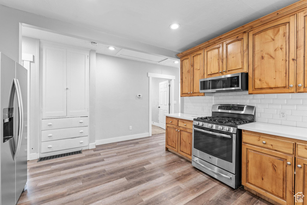 Kitchen featuring stainless steel appliances, light countertops, tasteful backsplash, baseboards, and light wood-style flooring