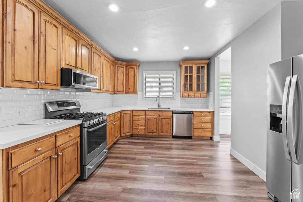 Kitchen with stainless steel appliances, wood finished floors, decorative backsplash, light countertops, and recessed lighting