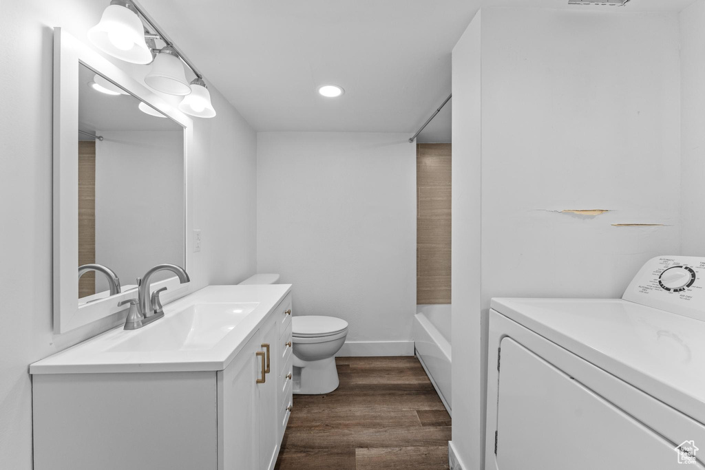 Bathroom featuring washer / dryer, wood finished floors, vanity, toilet, and recessed lighting