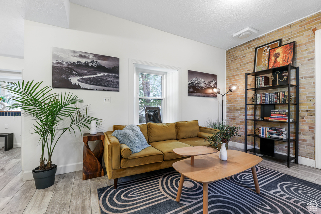 Living room featuring a textured ceiling, wood finished floors, baseboards, and brick wall