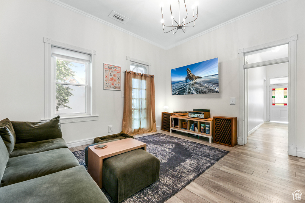 Living area with baseboards, an inviting chandelier, visible vents, crown molding, and wood finished floors