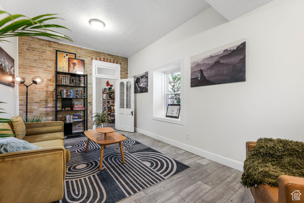 Living room featuring a textured ceiling, wood finished floors, baseboards, and brick wall