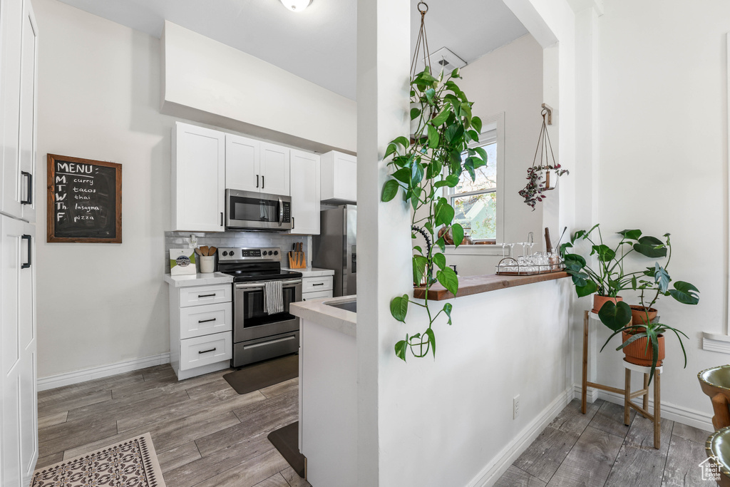 Kitchen with white cabinetry, light countertops, appliances with stainless steel finishes, and wood finished floors