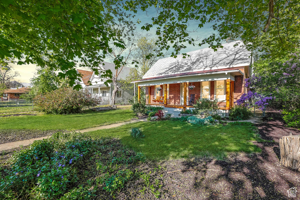 Back of house featuring a yard, brick siding, covered porch, and fence