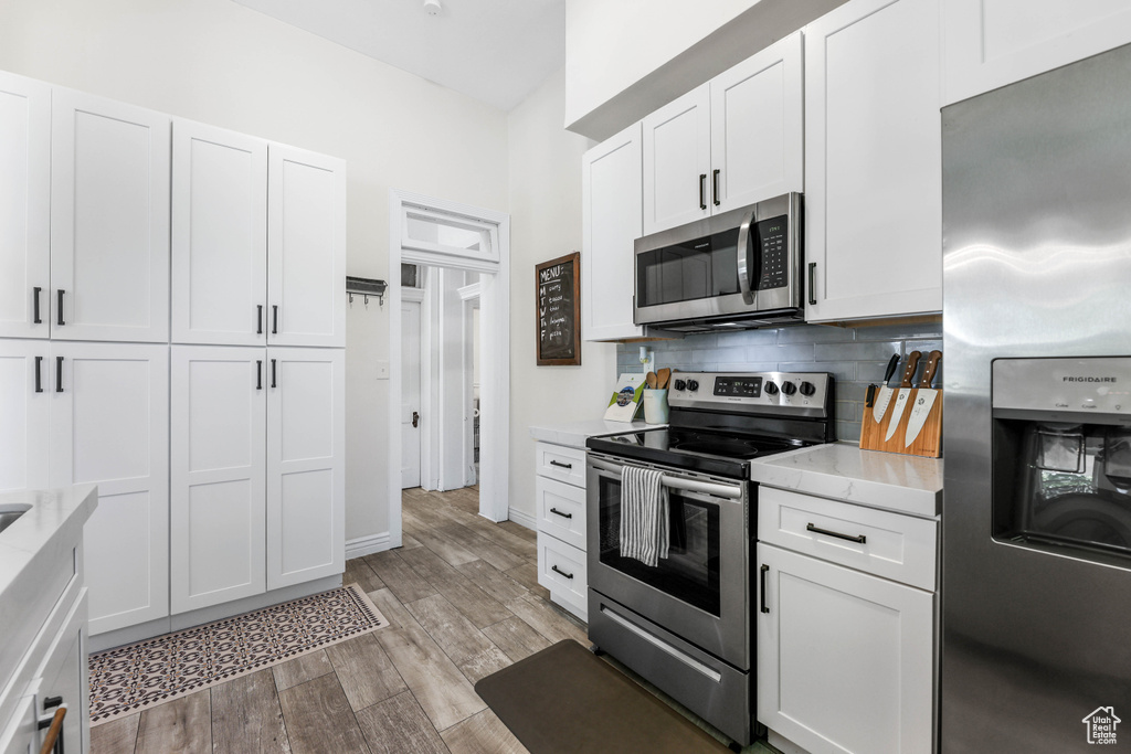 Kitchen with baseboards, decorative backsplash, light wood-style floors, white cabinets, and appliances with stainless steel finishes