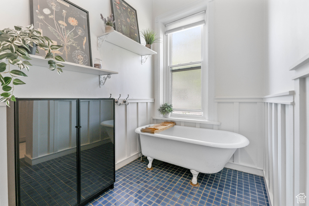 Bathroom featuring tile patterned floors, a decorative wall, a freestanding tub, and a wainscoted wall