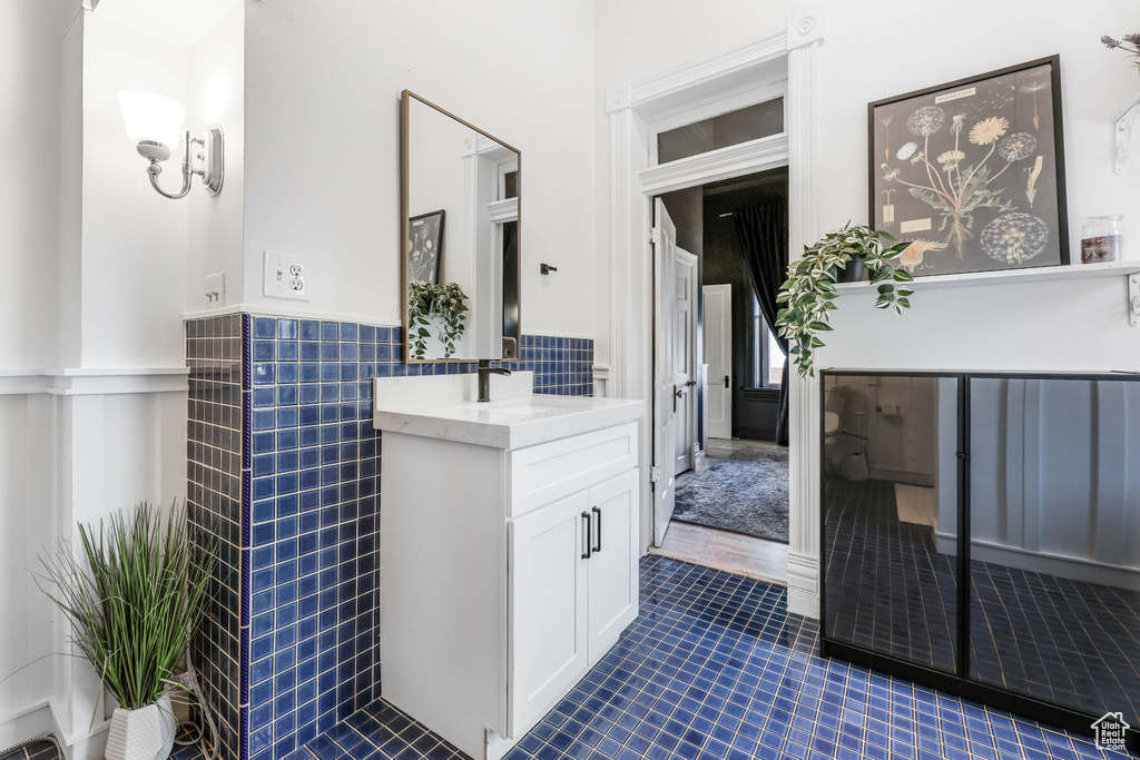 Bathroom with tile walls, tile patterned floors, vanity, and a wainscoted wall