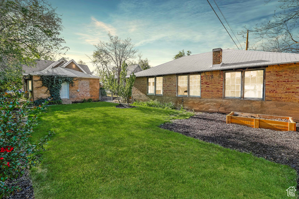 Rear view of property with a yard, a shingled roof, a chimney, and brick siding