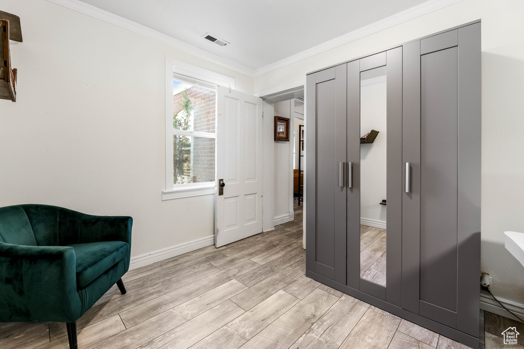 Living area with crown molding, light wood-type flooring, visible vents, and baseboards