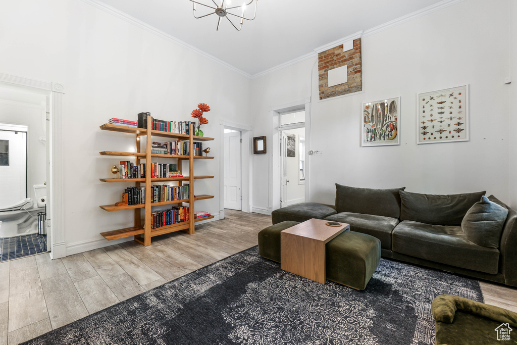 Living area with baseboards, ornamental molding, a chandelier, a towering ceiling, and wood finished floors