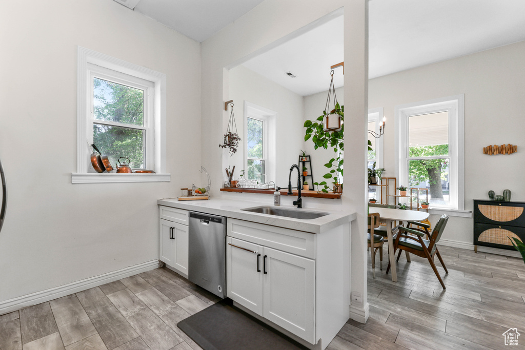 Kitchen featuring a sink, light wood-type flooring, dishwasher, white cabinetry, and light countertops