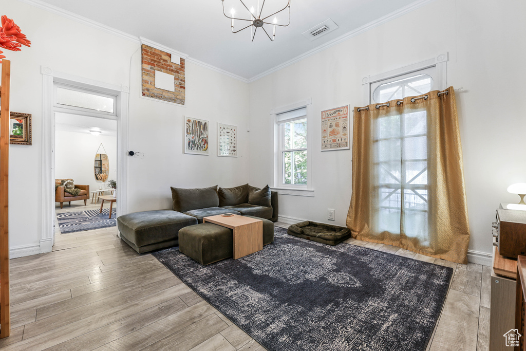 Living area featuring wood finished floors, a notable chandelier, crown molding, visible vents, and baseboards