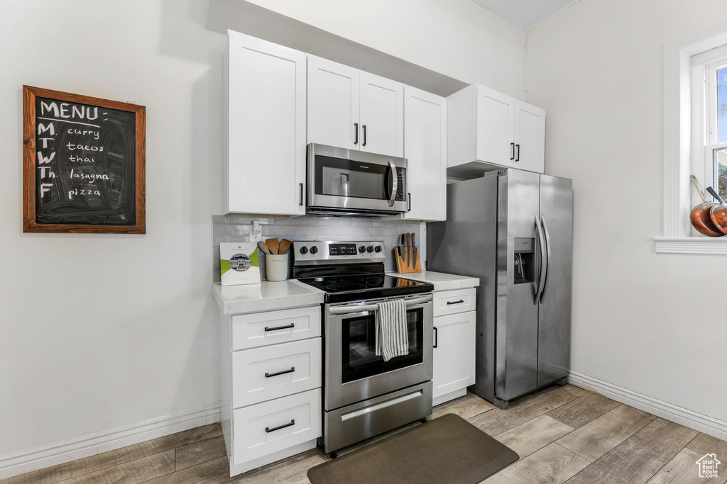 Kitchen featuring light wood finished floors, light countertops, stainless steel appliances, and baseboards
