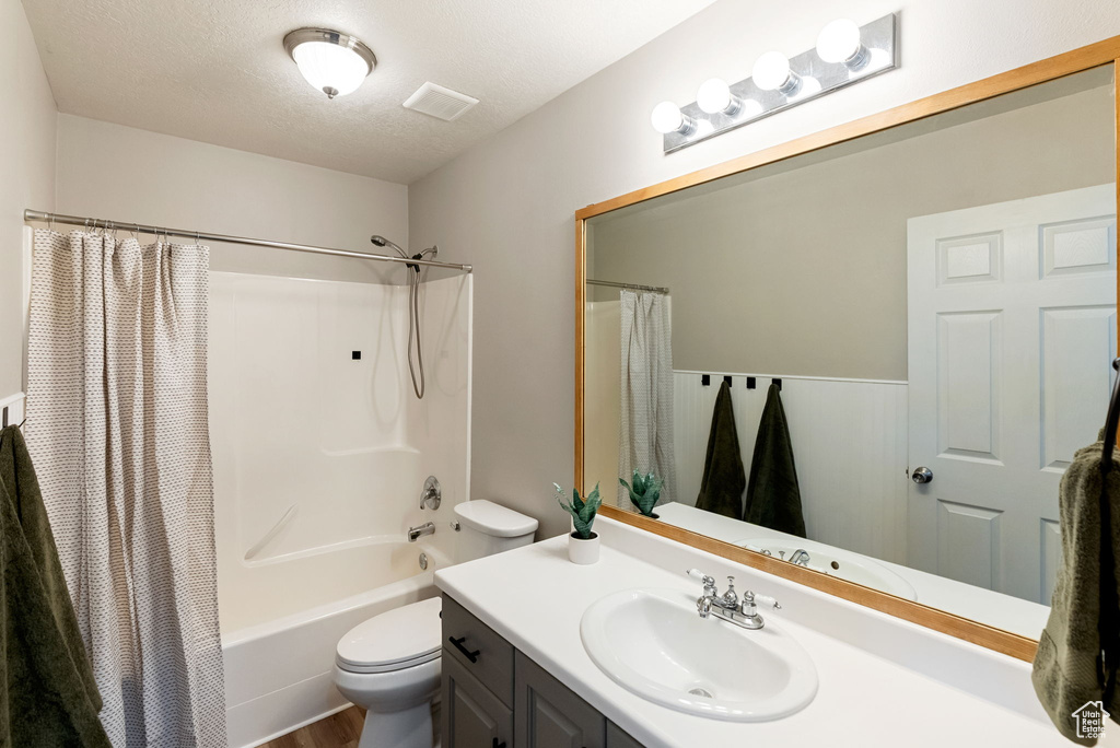 Full bath featuring toilet, vanity, a textured ceiling, shower / tub combo with curtain, and wood finished floors