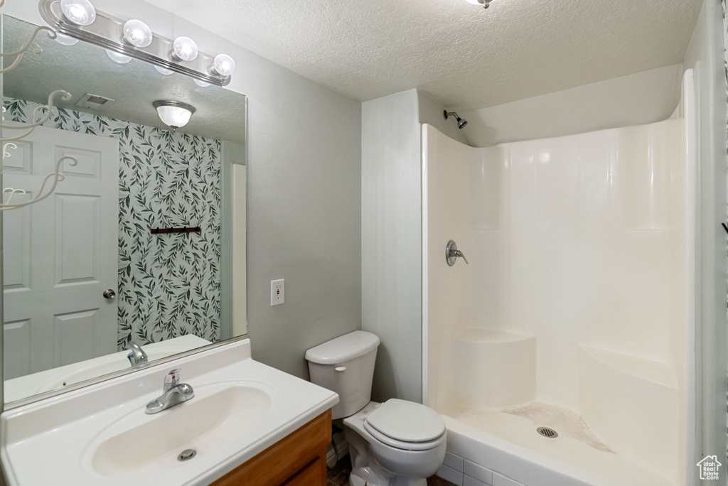 Full bathroom with a textured ceiling, toilet, a shower, and vanity