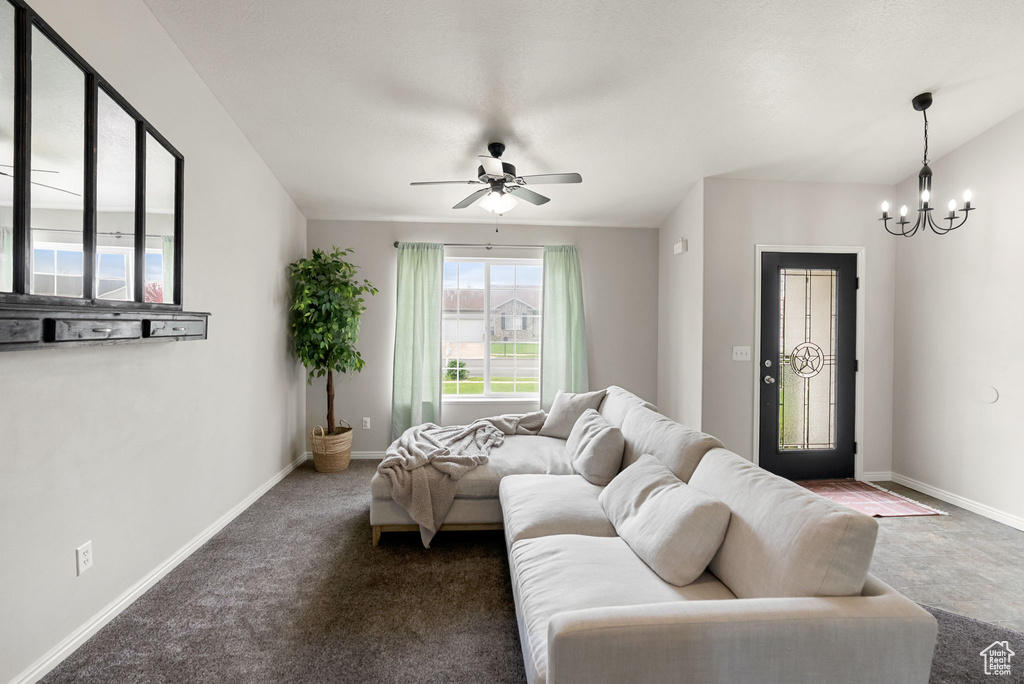 Carpeted living room with a chandelier, ceiling fan, and baseboards