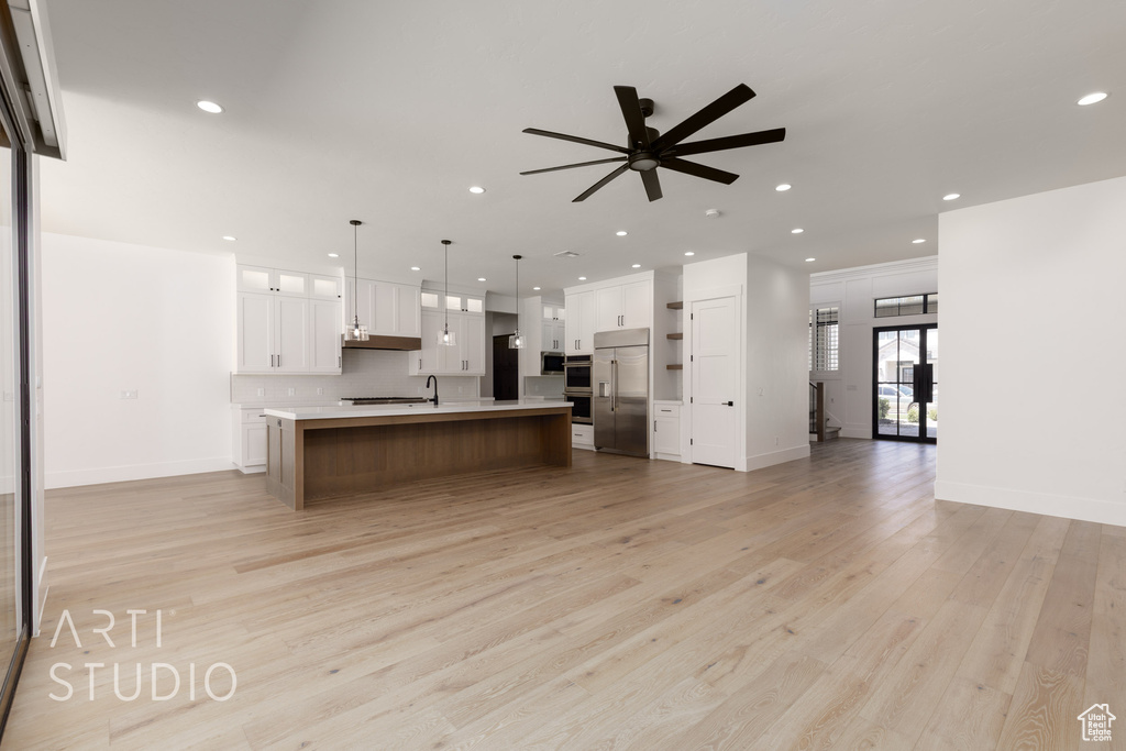 Kitchen featuring stainless steel appliances, open floor plan, light countertops, ceiling fan, and light wood-style floors