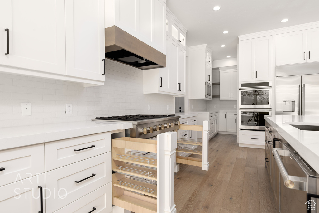 Kitchen with stainless steel appliances, under cabinet range hood, recessed lighting, light wood-style flooring, and white cabinetry
