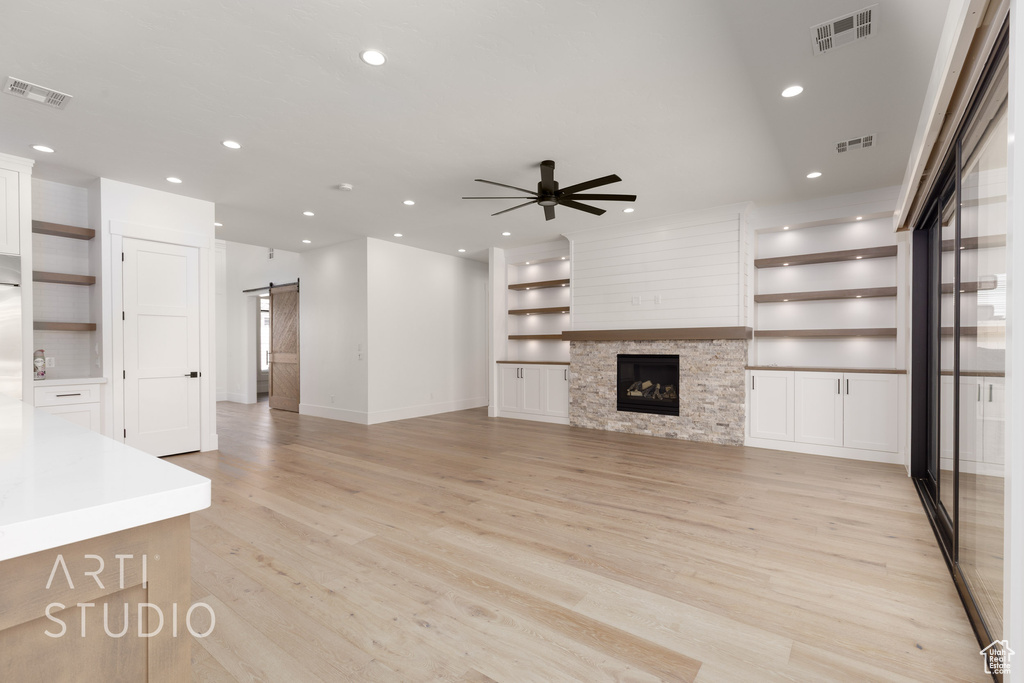 Unfurnished living room featuring a barn door, a ceiling fan, light wood finished floors, recessed lighting, and built in features