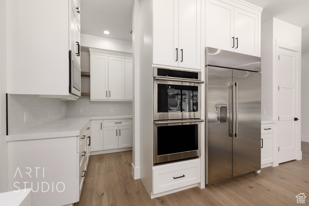 Kitchen with stainless steel appliances, light wood finished floors, white cabinetry, backsplash, and light countertops