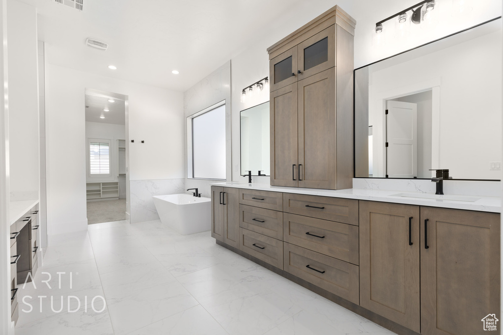 Full bath with a soaking tub, double vanity, marble finish flooring, and recessed lighting