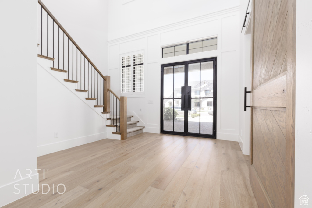 Entryway with stairway, french doors, light wood finished floors, a towering ceiling, and baseboards