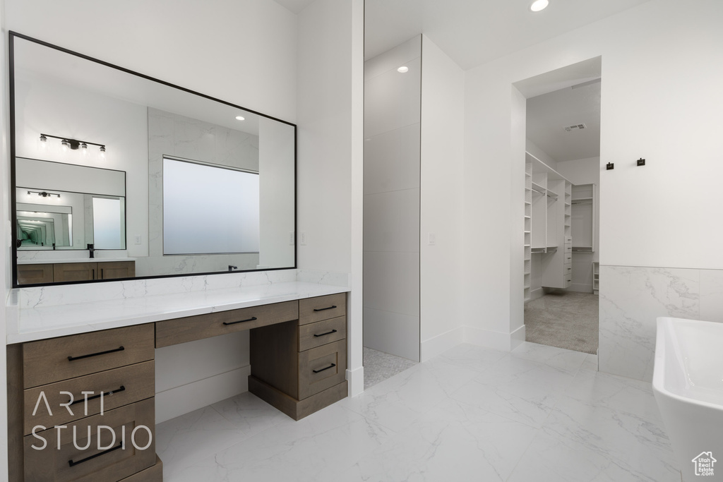 Bathroom with marble tiled floors, a freestanding bath, vanity, a walk in closet, and recessed lighting