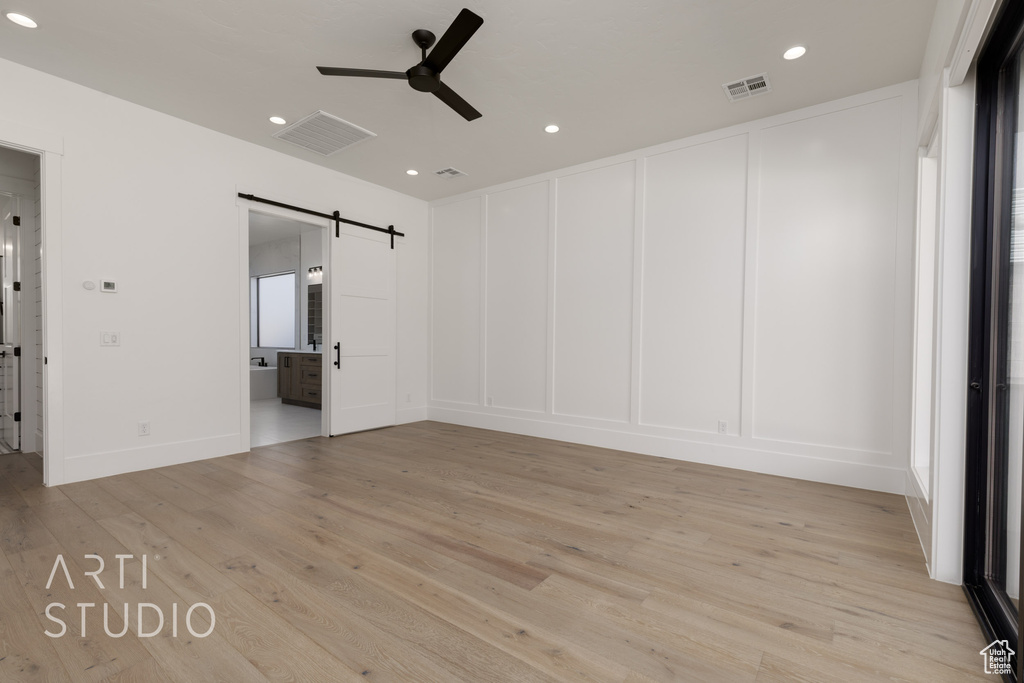 Unfurnished bedroom with a barn door, a decorative wall, recessed lighting, light wood-style floors, and connected bathroom