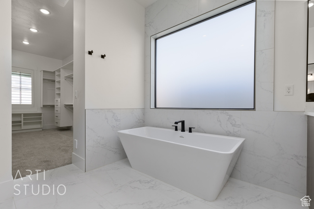Full bathroom featuring marble finish flooring, tile walls, a freestanding tub, and recessed lighting