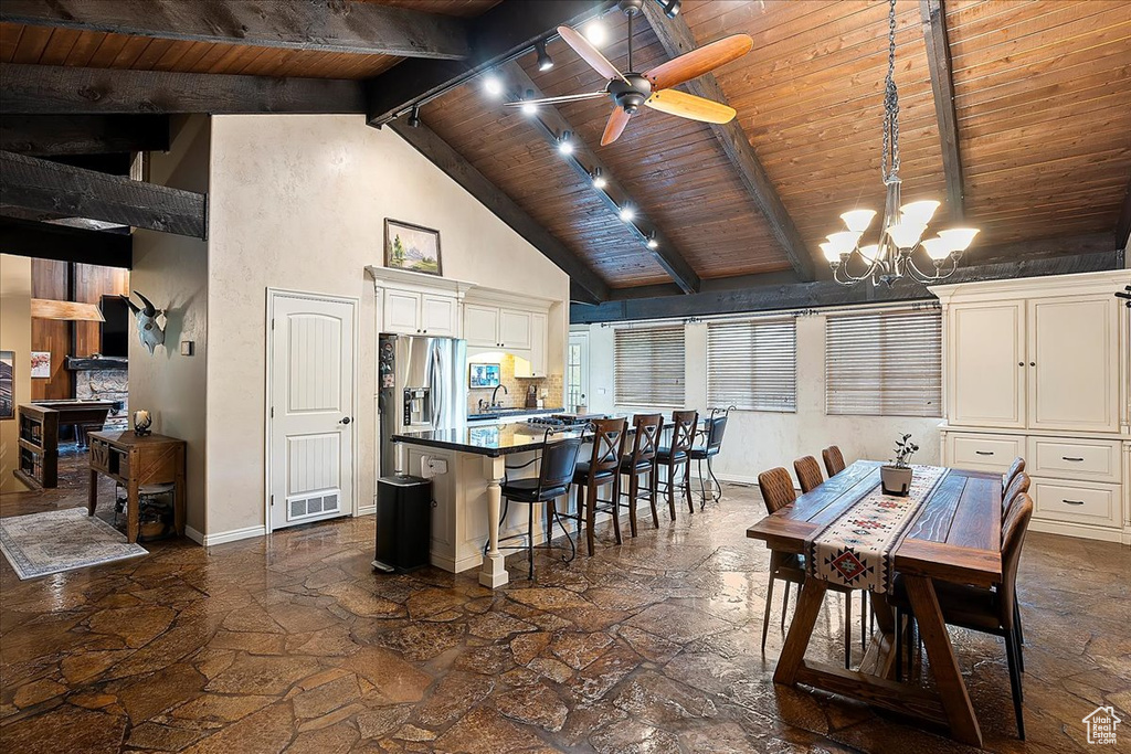 Dining space with stone floors, wooden ceiling, a chandelier, high vaulted ceiling, and beam ceiling