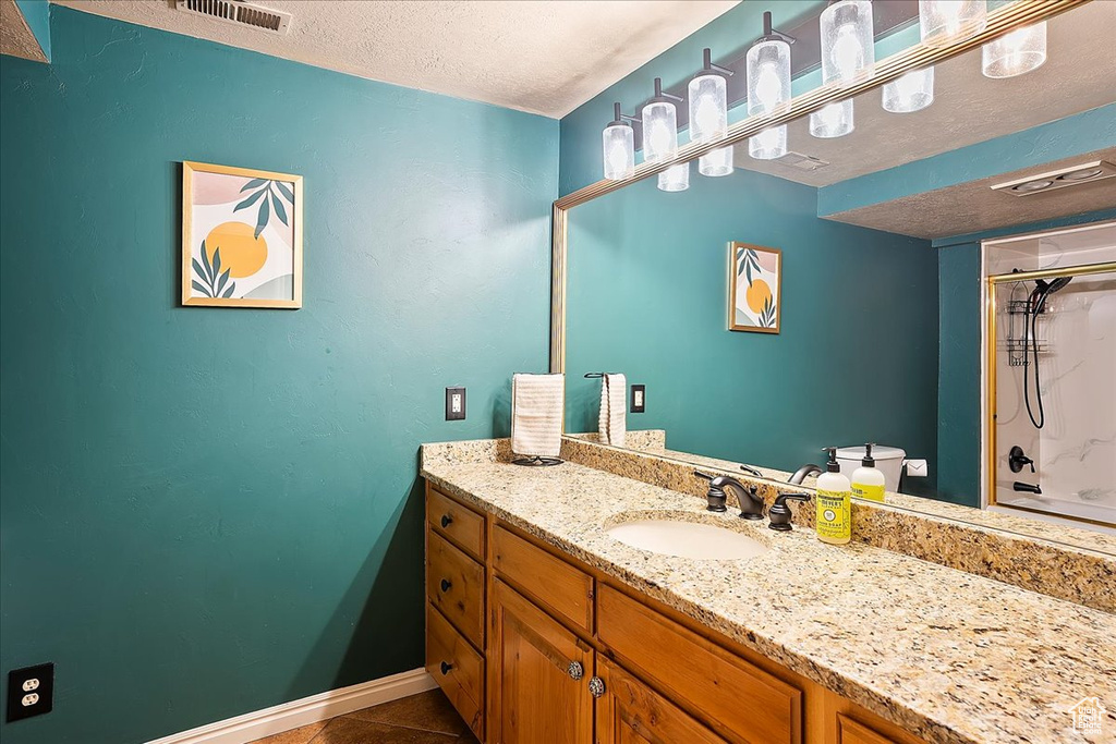 Bathroom with a shower, a textured ceiling, vanity, tile patterned floors, and baseboards