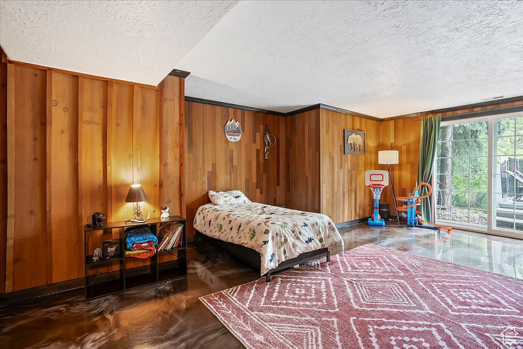 Bedroom with access to outside, a textured ceiling, wooden walls, and ornamental molding