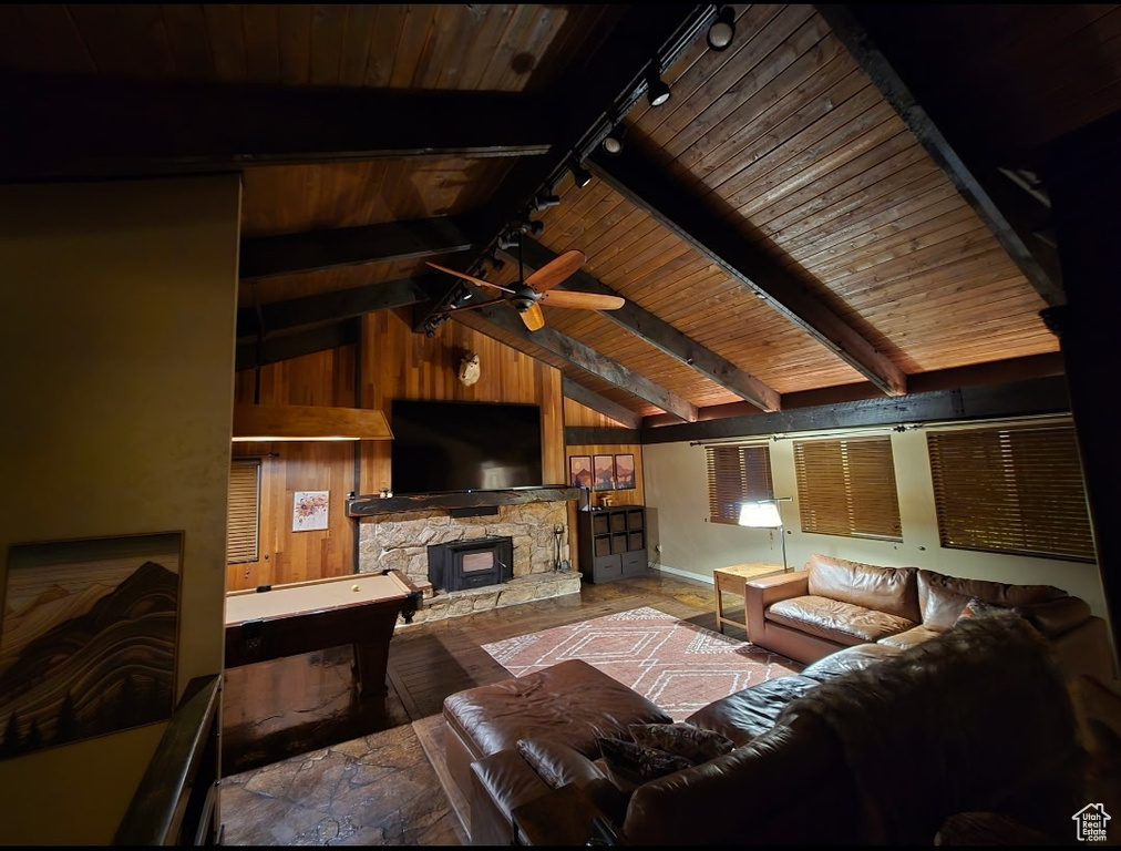 Living area featuring rail lighting, wooden walls, wooden ceiling, a ceiling fan, and a stone fireplace