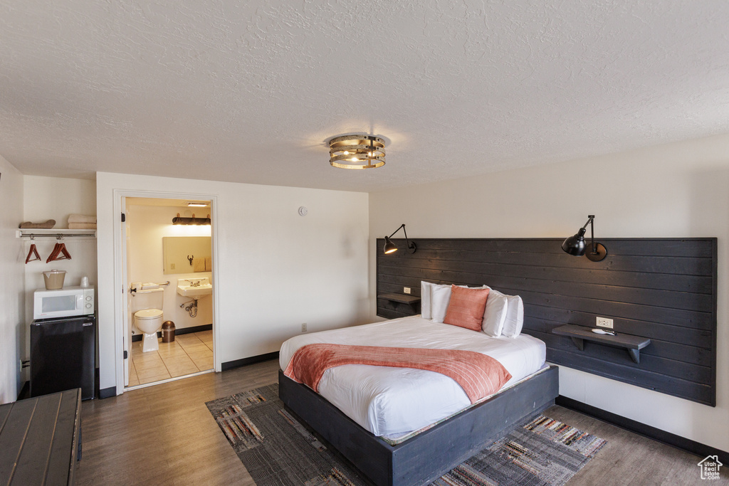 Bedroom featuring wood finished floors, a textured ceiling, baseboards, and ensuite bath