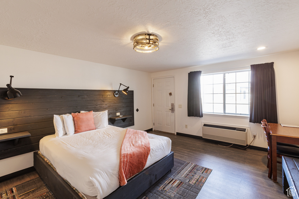 Bedroom featuring dark wood-style flooring, a wall mounted AC, a textured ceiling, baseboards, and recessed lighting
