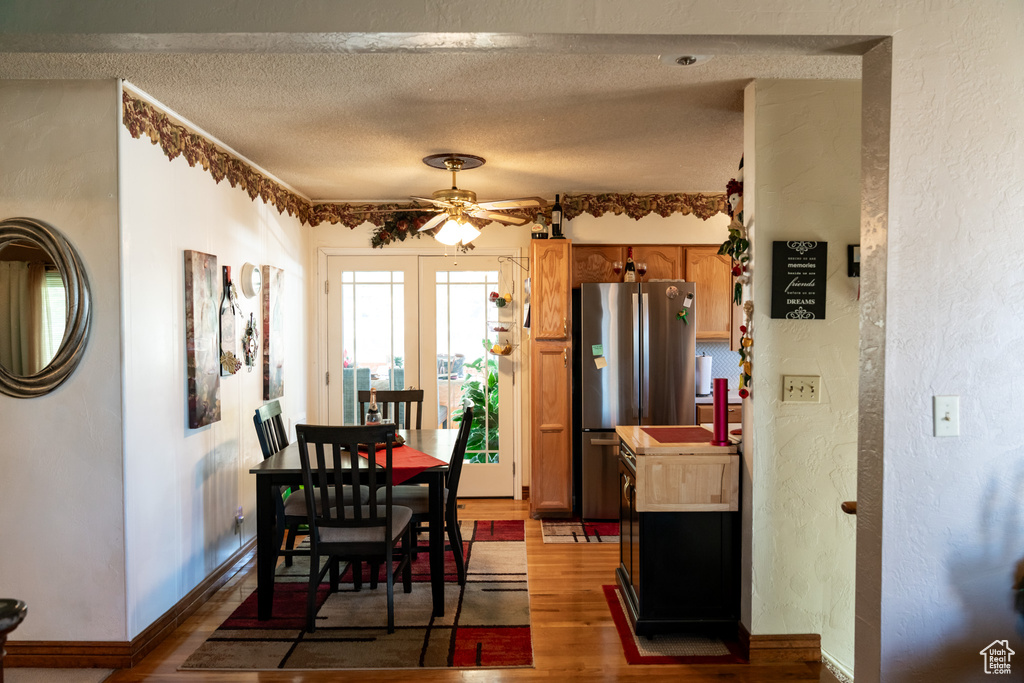 Dining space with wood finished floors, ceiling fan, a textured wall, a textured ceiling, and french doors