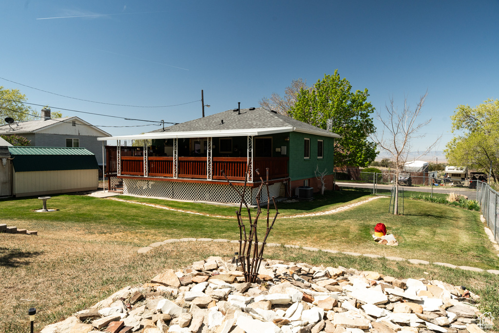 Back of property with a storage shed, a wooden deck, an outbuilding, a shingled roof, and central AC unit