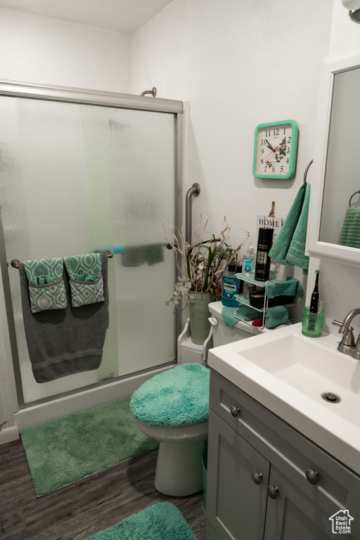 Bathroom featuring wood finished floors, a shower stall, vanity, and toilet