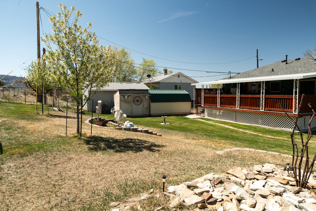 View of grassy yard with a storage shed, a wooden deck, and an outdoor structure
