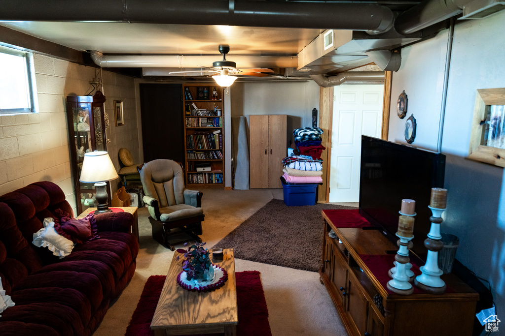 Carpeted living room with ceiling fan and concrete block wall