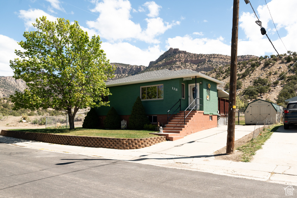 View of front of home featuring a shed, a mountain view, an outbuilding, concrete driveway, and a front yard
