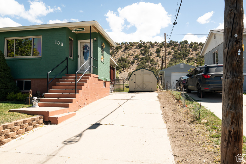 View of front of property with driveway, an outdoor structure, a detached garage, a storage unit, and a mountain view