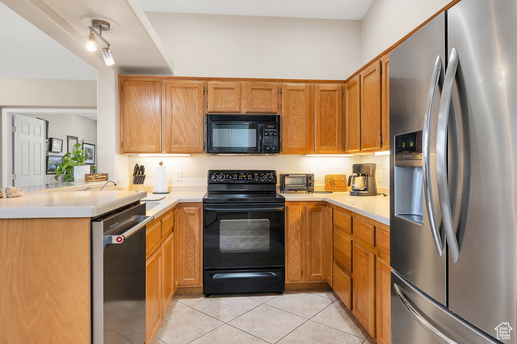 Kitchen with black appliances, light tile patterned flooring, light countertops, and a peninsula