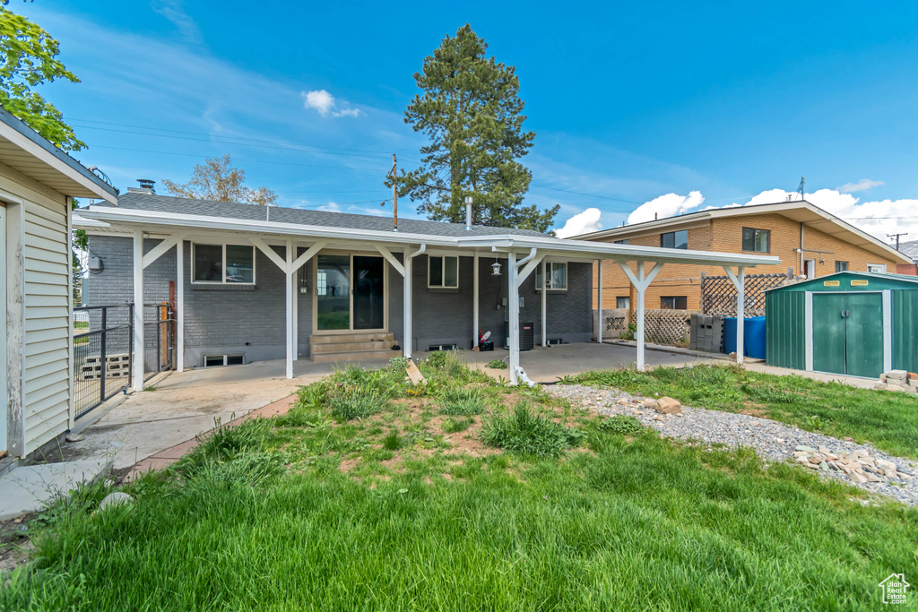 Back of property featuring brick siding, a shed, an outbuilding, a patio area, and a yard