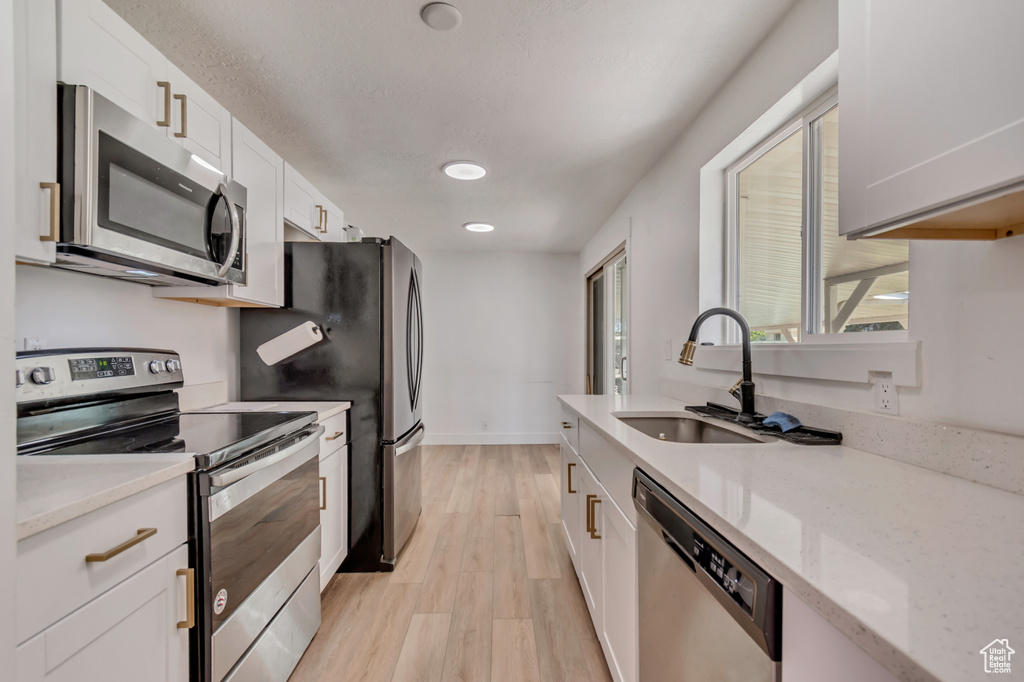 Kitchen featuring light wood-type flooring, recessed lighting, white cabinets, a sink, and appliances with stainless steel finishes