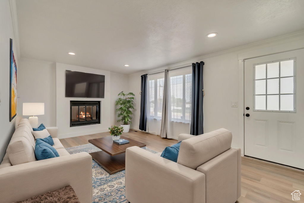 Living area featuring recessed lighting, ornamental molding, a lit fireplace, and light wood-type flooring