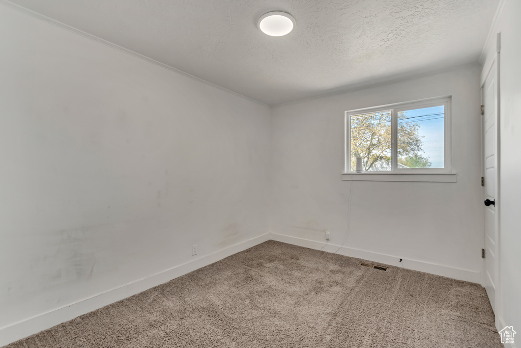 Empty room with carpet flooring, a textured ceiling, baseboards, and visible vents