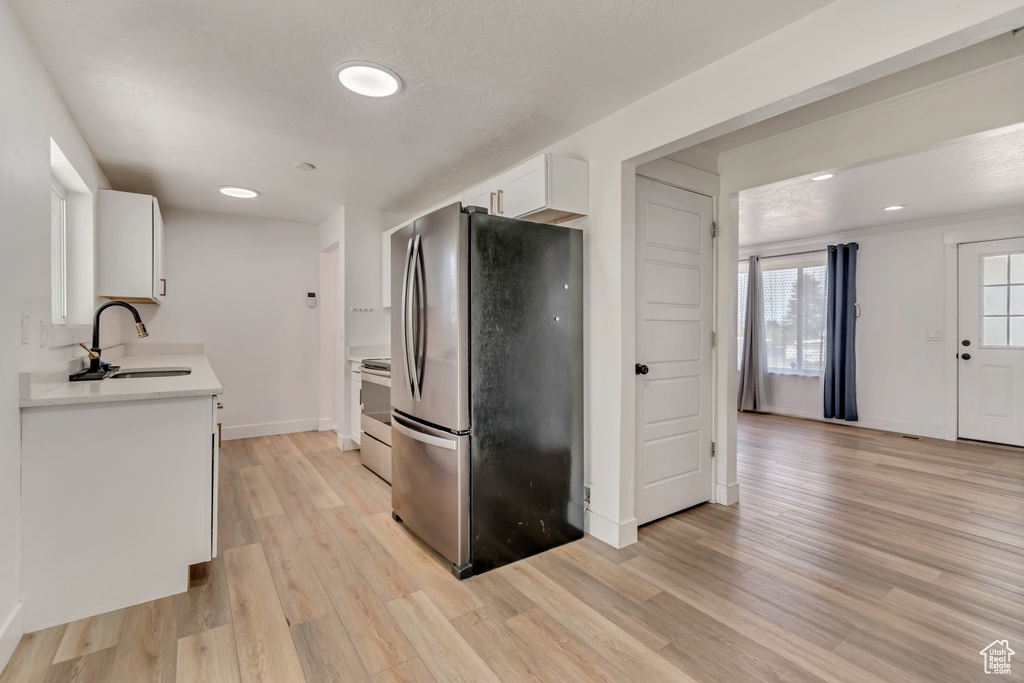 Kitchen with electric range, a sink, light wood-style floors, light countertops, and freestanding refrigerator