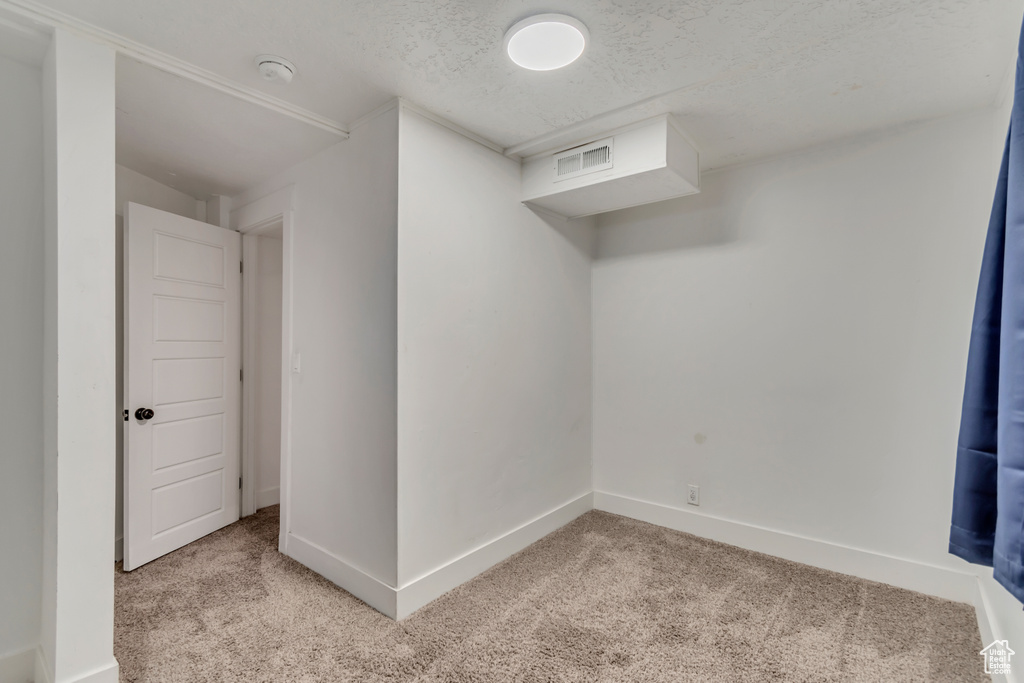 Finished below grade area featuring a textured ceiling, baseboards, light colored carpet, and visible vents